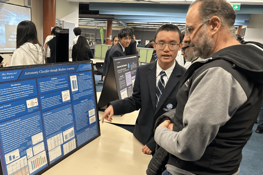 A student talking to another visitor, standing in front of a poster display