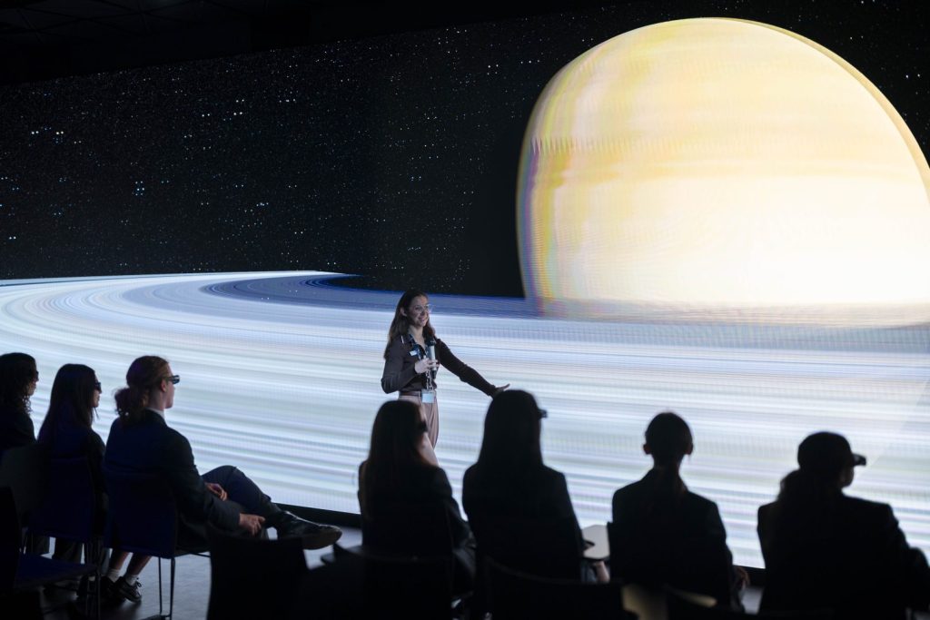 A group of students sitting and listening to a lecture talk in a dark studio featuring a 100-square-metre stereoscopic LED wall