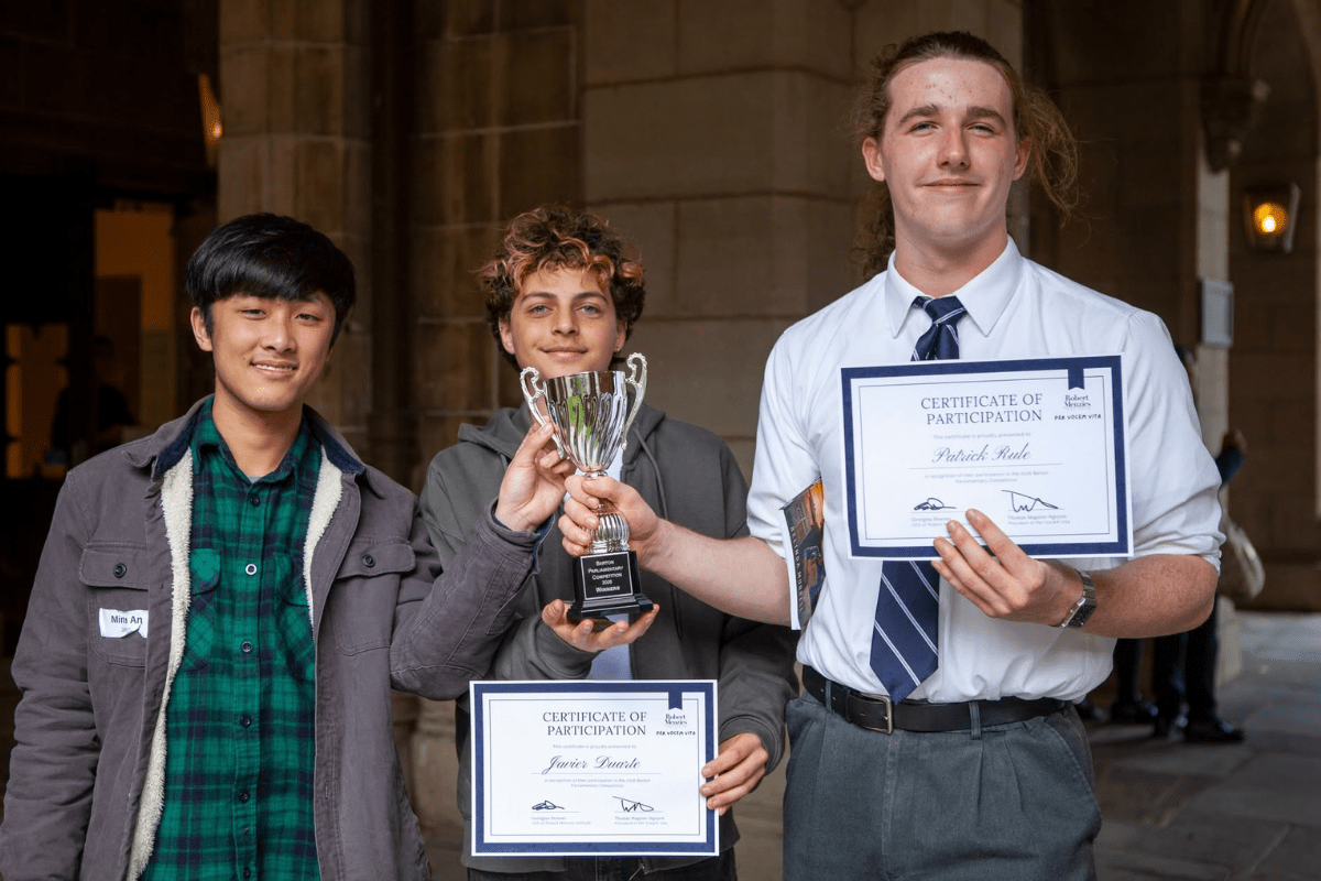 Three male students holding a trophy together, smiling