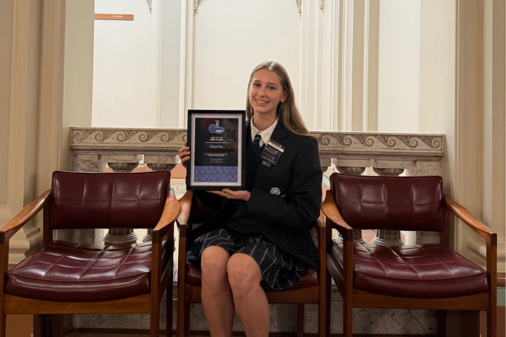 A young female student sitting and holding an award certificate 